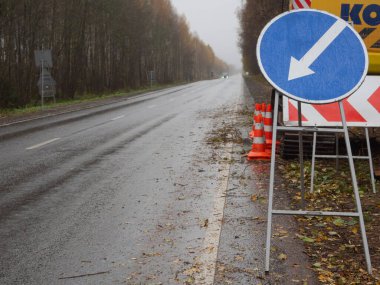 Sağdaki servis yolu tabelası. Yolda geçici trafik işaretleri var. Yolların onarımı