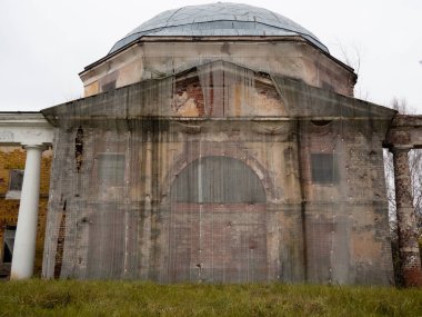 Şeffaf bir kumaşla kaplı harap olmuş eski bir tuğla bina. Sütunlu acil servis..