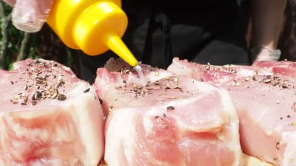男性の手袋をはめた手はフライパンに豚肉のステーキに油を注ぐ.グリル用の肉料理 — ストック動画