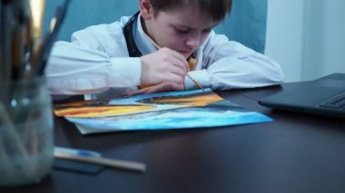 Tişörtlü ve kulaklı bir çocuk boya fırçasıyla resim çiziyor.