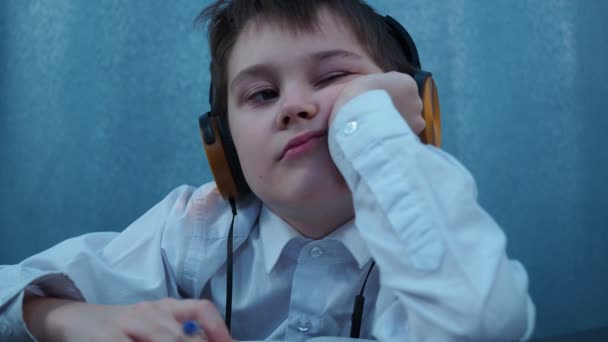 Un ragazzo in camicia e cuffie sta pensando con la testa appoggiata sulla mano — Video Stock