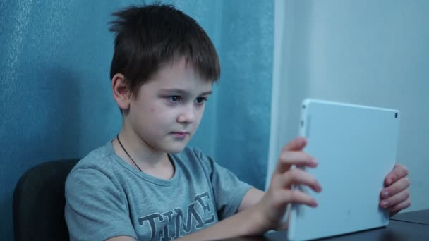 Ein Junge im T-Shirt studiert auf einem weißen Tablet, das an einem Tisch sitzt — Stockvideo