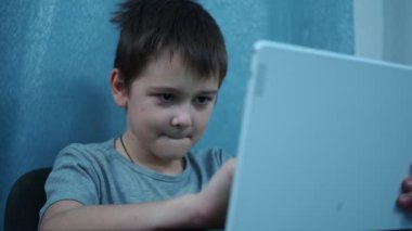 Çocuk masada oturan beyaz bir tablette okuyor.