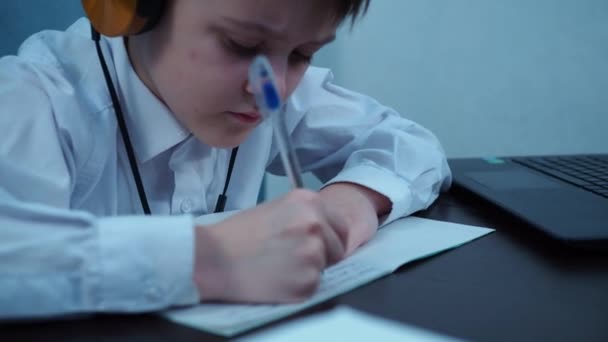 Kafasını eline dayamış tişörtlü bir çocuk deftere yazıyor. — Stok video