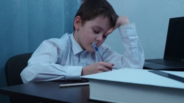 Ένα αγόρι με ένα πουκάμισο με το κεφάλι του καρφωμένο στο χέρι του γράφει σε ένα σημειωματάριο. — Αρχείο Βίντεο