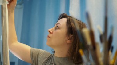 Genç bir kadın tuvale fırçayla resim çiziyor.