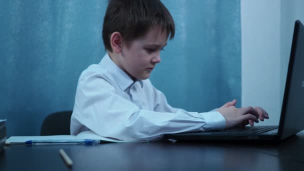 Een jongen in een shirt typt op de sleutels van een laptop. draaien, glimlacht hij — Stockvideo