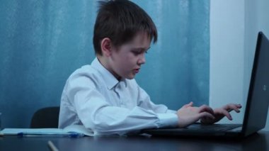 Tişörtlü bir çocuk dizüstü bilgisayarın anahtarlarını yazıyor.