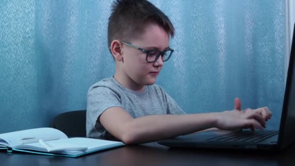 A boy with glasses types on a computer, turns around, laughs and smiles. remote study — ストック動画