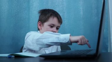 Gömlekli bir çocuk masada oturan bir dizüstü bilgisayarın anahtarlarını daktilo ediyor. Çocuklar öğrenmek yerine oynarlar.