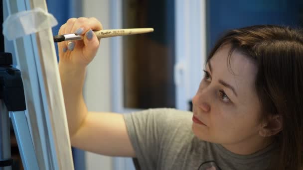 Молода жінка малює картину пензлем в студії — стокове відео