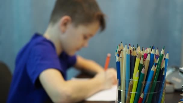 Мальчик рисует карандашами на бумаге. мальчик вне фокуса, карандаши на переднем плане — стоковое видео