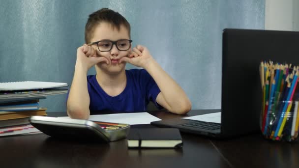 De jongen luistert naar een les op afstand op de computer. hij trekt gezichten en lacht om de monitor — Stockvideo