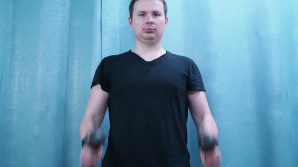 Een man in een zwart t-shirt doet aan sport. tilt halters op de biceps. sporten thuis — Stockvideo