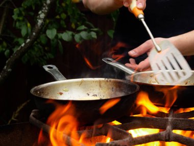 Kızartma tavasında ızgarada pişirmek. Kızartma tavası yanıyor. Bir adam kızartma tavasında yemek karıştırır.