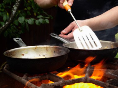 doğada piknik. Kızartma tavası yanıyor. Bir adam kızartma tavasında yemek pişiriyor.