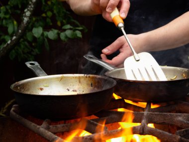 doğada piknik. Kızartma tavası yanıyor. Bir adam kızartma tavasında yemek pişiriyor.