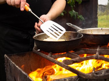 Kızartma tavasında ızgarada pişirmek. Kızartma tavası yanıyor. Bir adam kızartma tavasında yemek karıştırır.