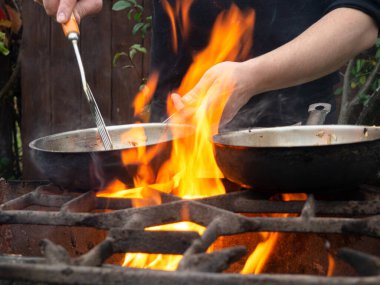 Kızartma tavasında ızgarada pişirmek. Kızartma tavası yanıyor. Bir adam kızartma tavasında yemek karıştırır.