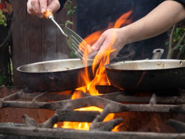Kızartma tavasında ızgarada pişirmek. Kızartma tavası yanıyor. Bir adam kızartma tavasında yemek karıştırır.