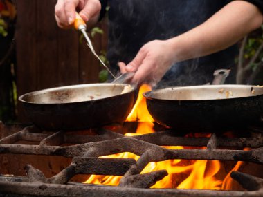 Kızartma tavasında ızgarada pişirmek. Kızartma tavası yanıyor. Bir adam kızartma tavasında yemek karıştırır.