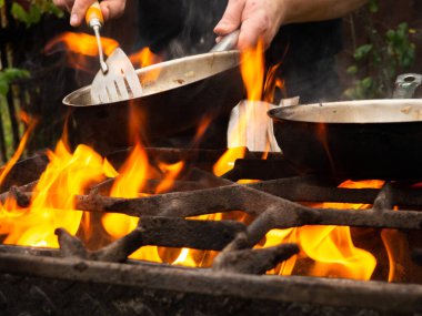 Kızartma tavasında ızgarada pişirmek. Kızartma tavası yanıyor. Bir adam kızartma tavasında yemek karıştırır.