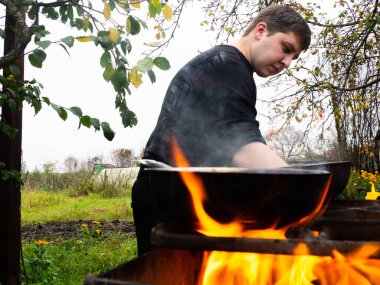 Ateşin içinden fotoğraf çekmek. Bir adam yanan bir barbekü için yemek hazırlar. Kızartma tavasında ızgarada pişirmek