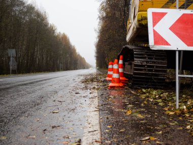 Sağdaki servis yolu tabelası. Yolun kenarında özel ekipman var. Yolda geçici trafik işaretleri var. Yolların onarımı.