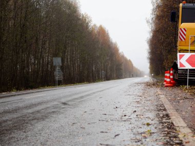 Sağdaki servis yolu tabelası. Yolun kenarında özel ekipman var. Yolda geçici trafik işaretleri var. Yolların onarımı.