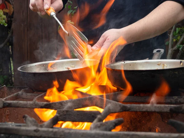 cooking on the grill in a frying pan. frying pan on fire. a man stirs food in a frying pan