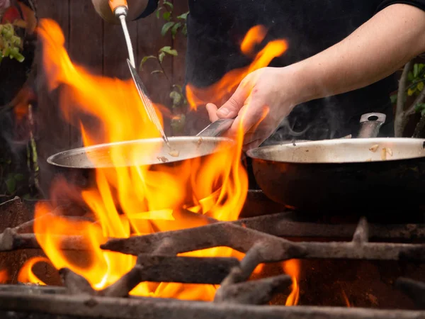 用煎锅在烤架上做菜 油锅着火了 一个人在煎锅里搅拌食物 — 图库照片