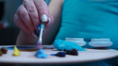 Kız paletten fırçayla boyayı karıştırıyor. Yakın çekim paleti. yan görünüm