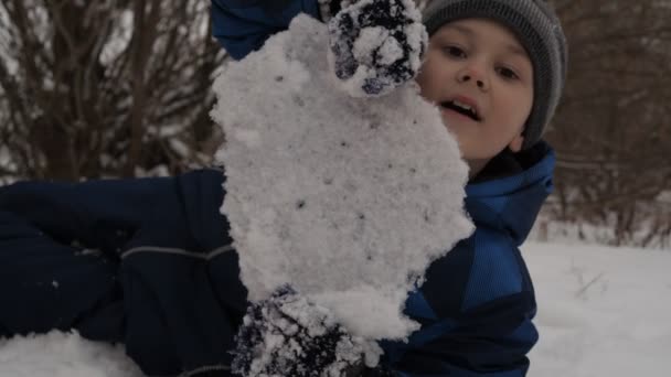 Le garçon prend un bloc de glace et le brise avec sa main comme dans un combat. les enfants jouent dans la neige — Video