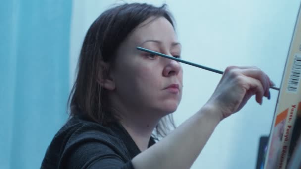 The artist draws a brush on a canvas standing on a tripod. home studio of fine arts. view of a girl with a bottom girl smiling at the camera — Stock Video