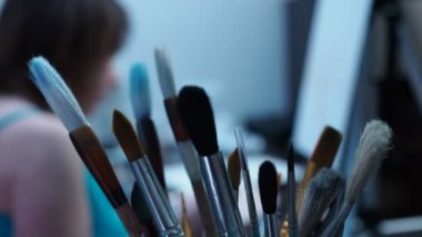 Yetenekli bir sanatçı tuval üzerinde fırçayla resim çizer. Püsküllerin arkasından bak. Odaklı fırçalar, odak dışı kız