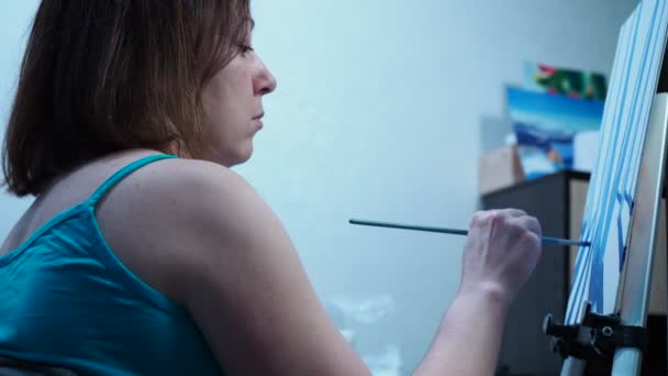 Uma menina desenha um pincel em uma tela de pé em um tripé. estúdio em casa de belas artes — Vídeo de Stock