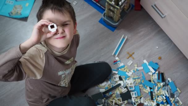 Een jongen speelt een bouwpakket van kunststof onderdelen op de vloer — Stockvideo