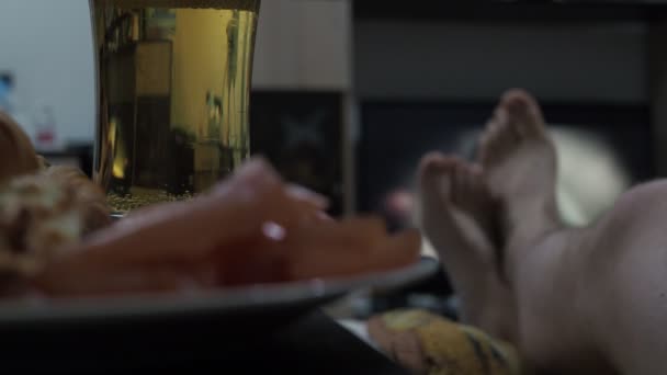 Μπύρα χύνεται σε ένα ποτήρι μπροστά από την τηλεόραση. mens πόδια και μια τηλεόραση εκτός εστίασης — Αρχείο Βίντεο