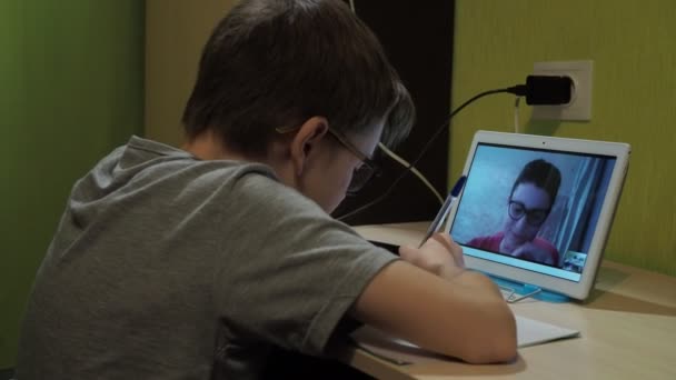 Μάθημα online. ένα αγόρι με γυαλιά κάθεται σε ένα τραπέζι.. ένας νεαρός δάσκαλος εξηγεί το πρόγραμμα — Αρχείο Βίντεο