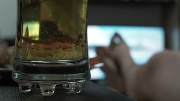 テレビの前のガラスの中のビール泡です。ソファに寝そべってる男 — ストック動画
