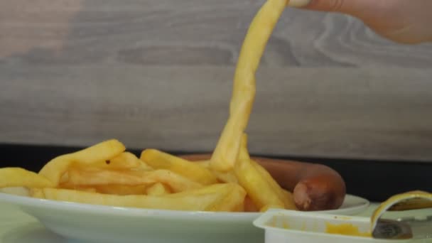 Um prato de batatas fritas e uma salsicha na mesa. uma mão das mulheres toma uma batata — Vídeo de Stock