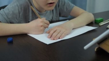 Gri tişörtlü bir çocuk tabletten bir kalemle resim çiziyor. Sanat dersleri çevrimiçi. Kamera modeli yakınlaştırıyor.
