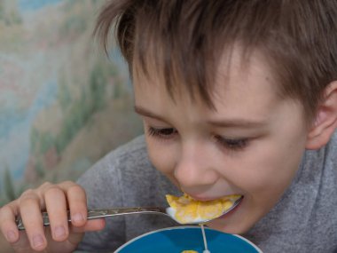 Çocuk mısır gevreğini bir kaşıkla sütle yiyor.