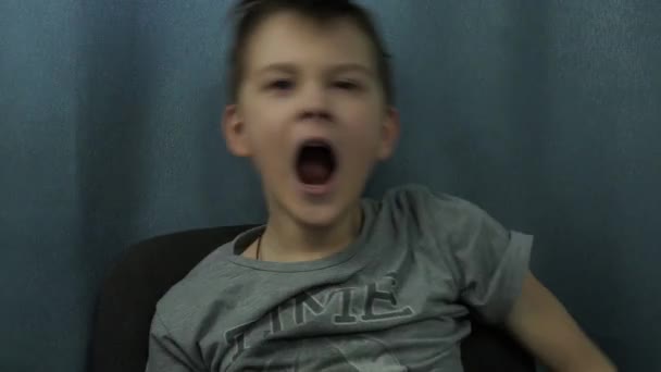 El niño bosteza sentado en una silla. parpadeando, tratando de despertar — Vídeos de Stock