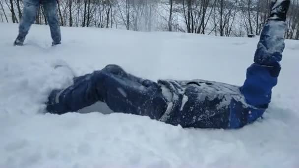 La familia juega bolas de nieve en invierno. un chico con una chaqueta azul yace en la nieve fresca y suave — Vídeos de Stock