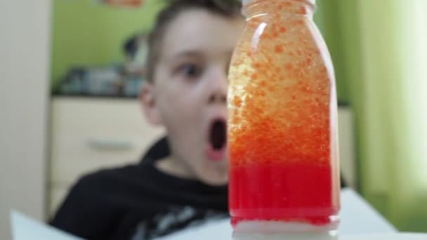 Der Junge führt zu Hause ein chemisches Experiment durch. Am Anfang liegt der Fokus auf der Flasche, danach auf dem überraschten Gesicht der Jungs. in der Flasche findet ein aktiver chemischer Prozess statt — Stockvideo