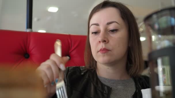 Een jonge vrouw die taart eet in een café. close-up van het gezicht — Stockvideo