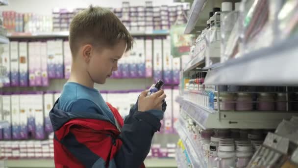 Een jongen in een rood jasje kiest verf op de toonbank. We kijken naar de potten met vloeistoffen. leest het etiket — Stockvideo