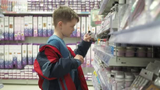赤いジャケットの少年がカウンターの上のペンキを選ぶ。瓶に液体が入っています。カウンターから様々な物を取り上げ — ストック動画