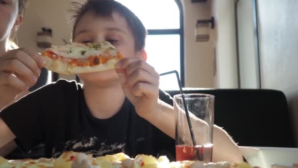 Un adolescent avec sa mère dans un café. garçon mange une grosse tranche de pizza — Video